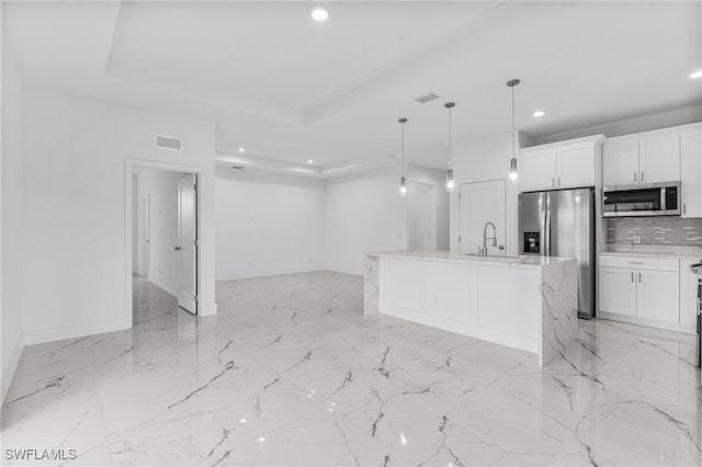 kitchen with white cabinets, stainless steel appliances, hanging light fixtures, and an island with sink