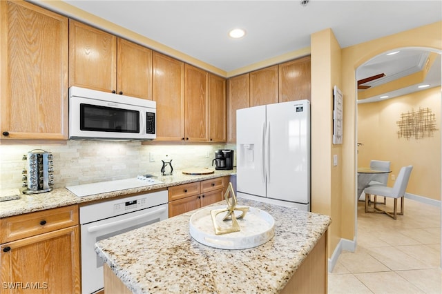 kitchen with light tile patterned floors, light stone counters, white appliances, backsplash, and a center island