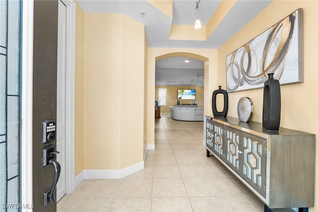 hallway featuring light tile patterned floors and a tray ceiling