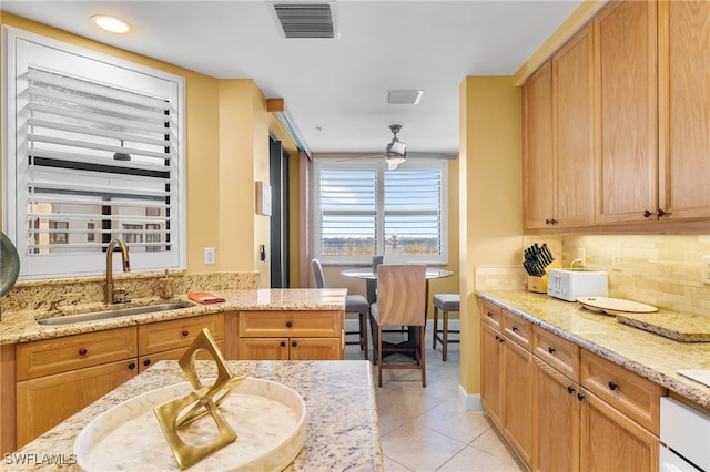 kitchen with tasteful backsplash, visible vents, light stone countertops, a sink, and light tile patterned flooring