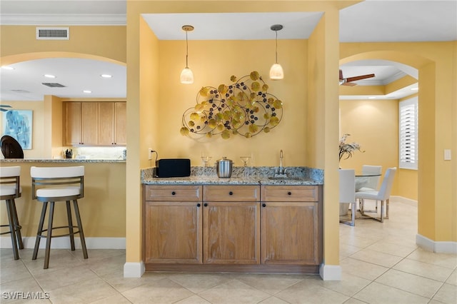 kitchen featuring light stone counters, arched walkways, crown molding, visible vents, and a ceiling fan