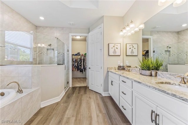 full bath featuring a stall shower, wood finished floors, a garden tub, a spacious closet, and a sink