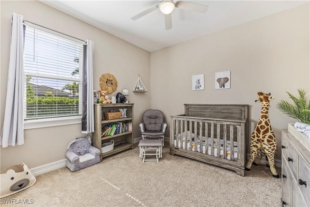 carpeted bedroom featuring a nursery area, a ceiling fan, and baseboards