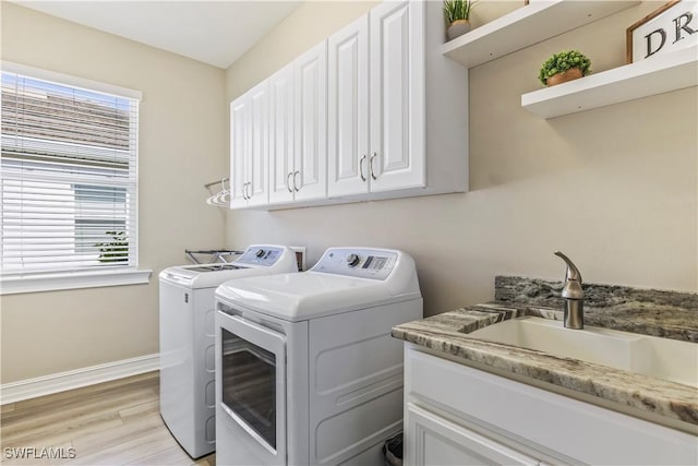 laundry room with light wood finished floors, cabinet space, baseboards, washing machine and clothes dryer, and a sink