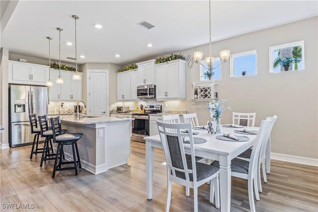 kitchen with a kitchen island with sink, white cabinetry, stainless steel appliances, and hanging light fixtures