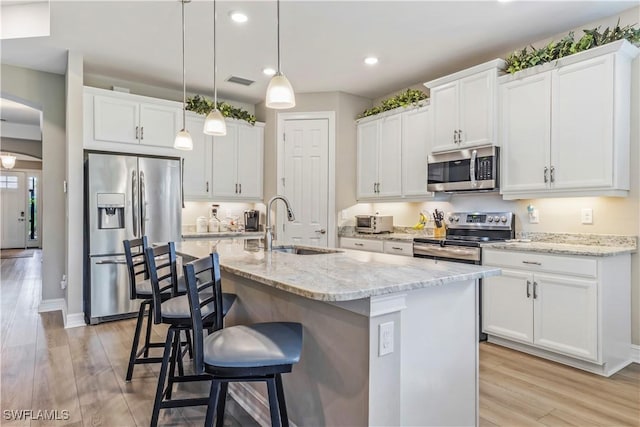 kitchen with light wood-type flooring, a kitchen bar, arched walkways, and stainless steel appliances