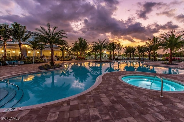 pool at dusk featuring a hot tub, a community pool, and a patio