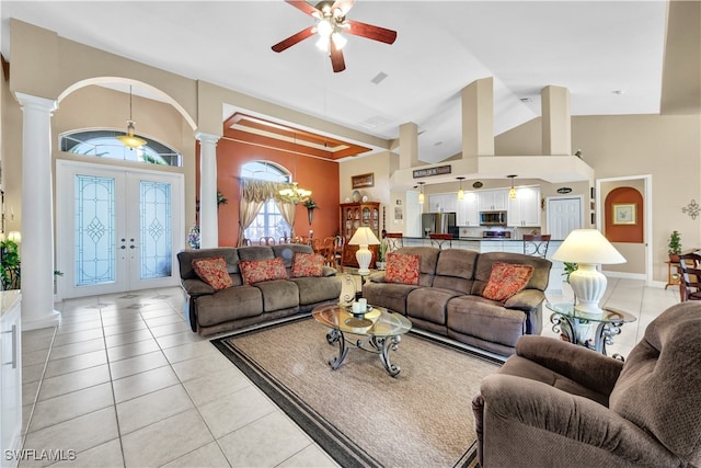 tiled living room featuring ceiling fan with notable chandelier, decorative columns, high vaulted ceiling, and french doors