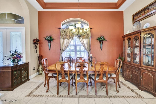 dining room with a towering ceiling, a raised ceiling, crown molding, light tile patterned floors, and a chandelier