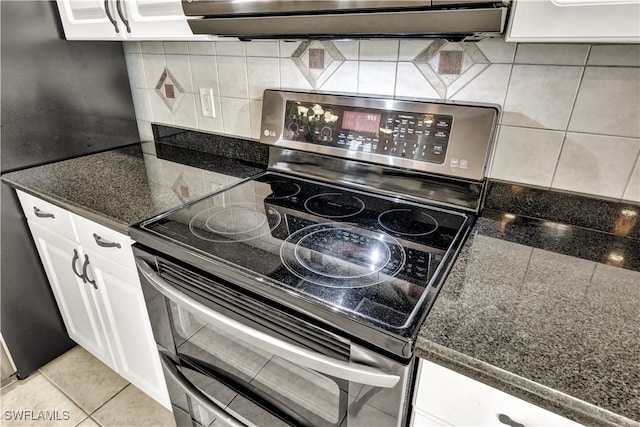 kitchen with electric range, light tile patterned floors, backsplash, dark stone counters, and white cabinets