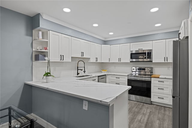 kitchen with a peninsula, a sink, appliances with stainless steel finishes, light wood-type flooring, and decorative backsplash