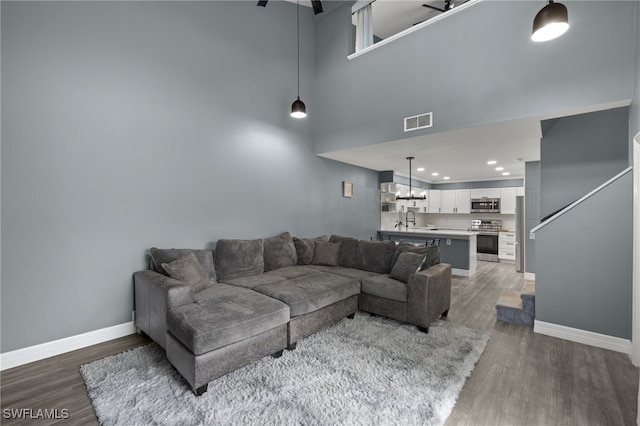 living room featuring dark hardwood / wood-style floors, ceiling fan, a towering ceiling, and sink