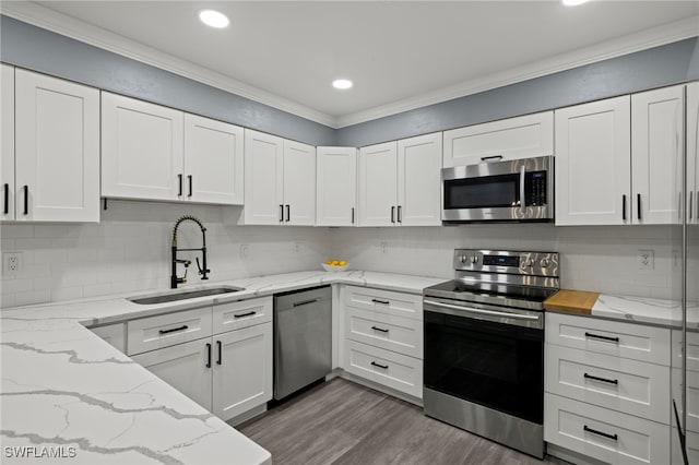 kitchen featuring sink, light stone counters, appliances with stainless steel finishes, white cabinets, and ornamental molding