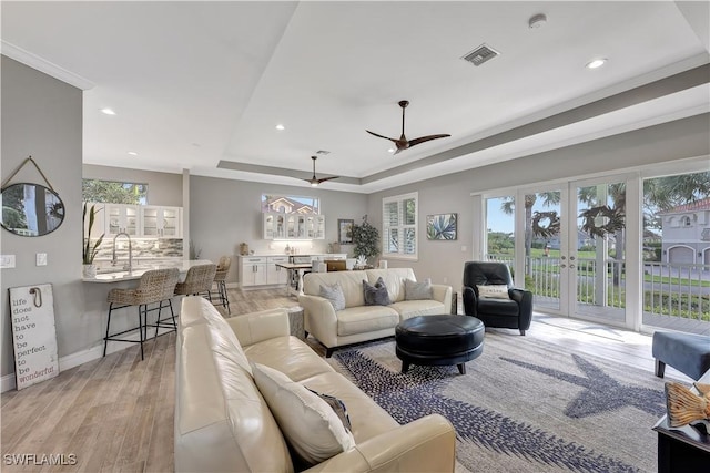 living area featuring french doors, a raised ceiling, visible vents, light wood-style floors, and baseboards