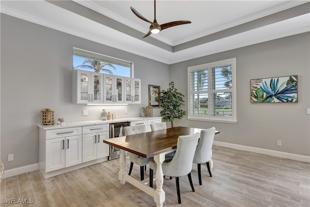 dining room featuring light hardwood / wood-style floors, ceiling fan, ornamental molding, and a tray ceiling