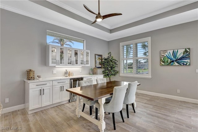 dining area with light wood-style flooring, ornamental molding, a raised ceiling, and baseboards