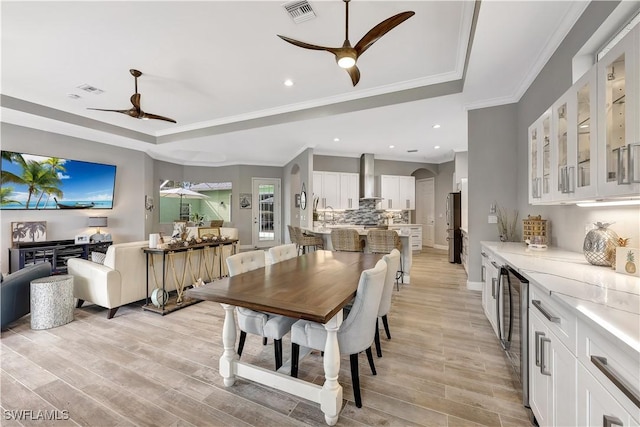 dining space with arched walkways, light wood-style flooring, visible vents, a ceiling fan, and a raised ceiling