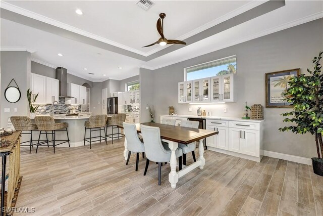 dining space featuring ornamental molding, light wood finished floors, a raised ceiling, and visible vents