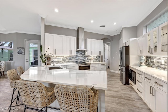 kitchen with stainless steel appliances, wall chimney range hood, a kitchen bar, white cabinetry, and a sink