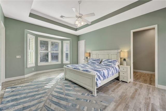 bedroom with ceiling fan, light wood-type flooring, and a tray ceiling