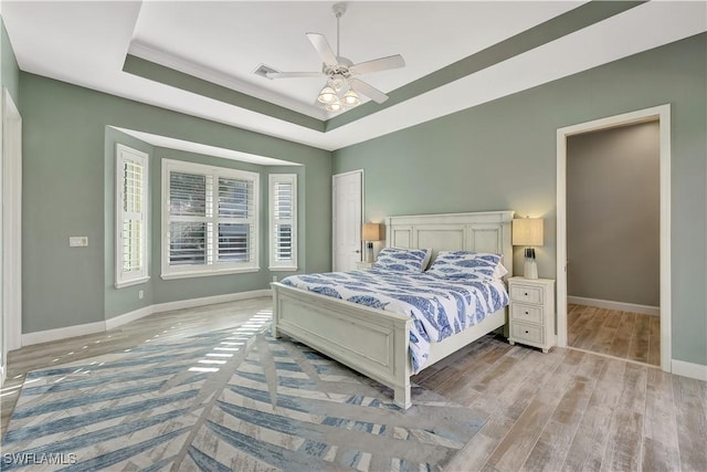 bedroom featuring a raised ceiling, visible vents, light wood-style flooring, a ceiling fan, and baseboards