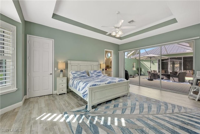 bedroom with baseboards, a tray ceiling, light wood-style flooring, and access to exterior