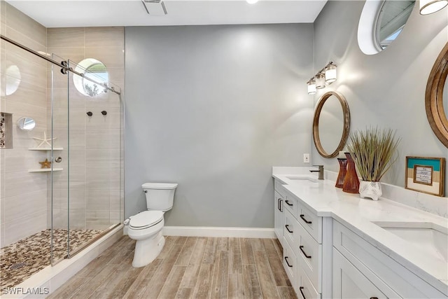 bathroom with toilet, wood finished floors, baseboards, double vanity, and a stall shower