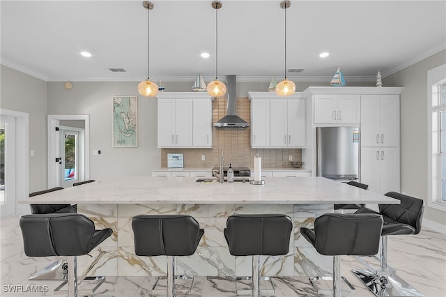 kitchen featuring a wealth of natural light, an island with sink, hanging light fixtures, and wall chimney range hood