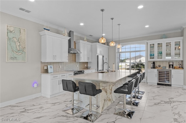 kitchen with hanging light fixtures, white cabinets, beverage cooler, and wall chimney range hood