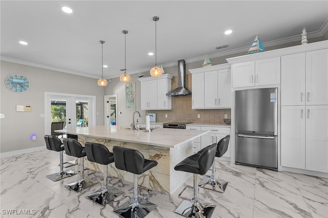 kitchen with white cabinetry, french doors, wall chimney exhaust hood, stainless steel fridge, and a kitchen island with sink