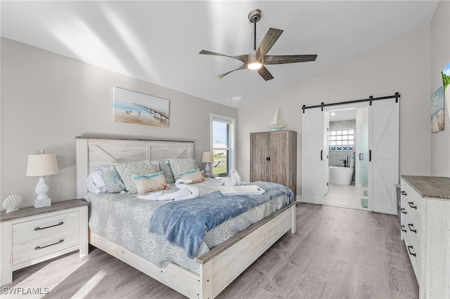 bedroom with a barn door, light hardwood / wood-style flooring, connected bathroom, and multiple windows