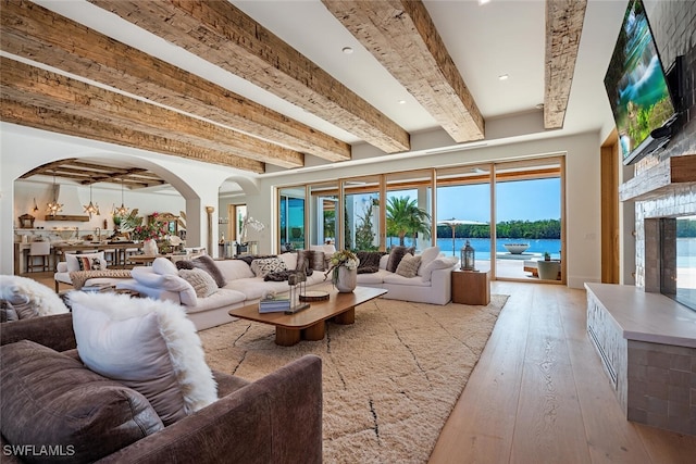 living room with arched walkways, beam ceiling, a water view, light wood-style floors, and a large fireplace