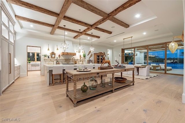 interior space with coffered ceiling, light wood-style flooring, a large island, a kitchen breakfast bar, and decorative light fixtures