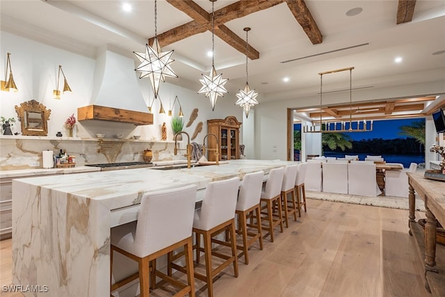 kitchen with a large island, light wood-style flooring, a breakfast bar area, hanging light fixtures, and a sink