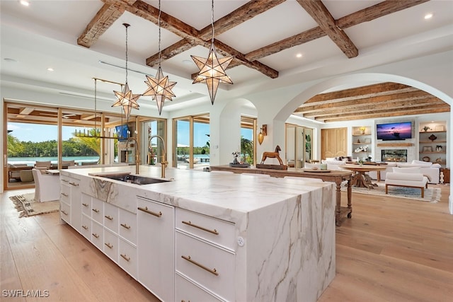 kitchen featuring light stone counters, a large island, hanging light fixtures, open floor plan, and white cabinets