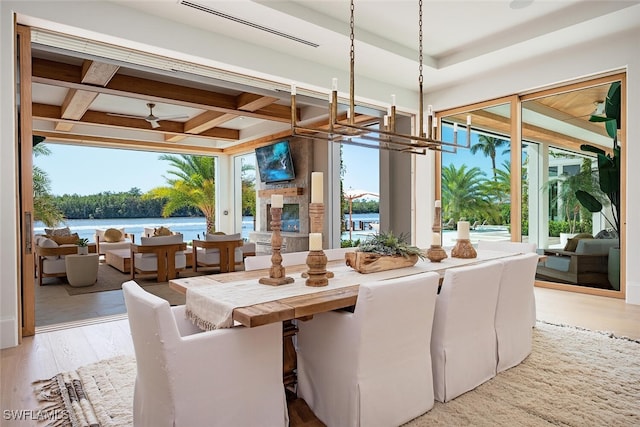 dining space with ceiling fan with notable chandelier, coffered ceiling, a fireplace, light wood-type flooring, and beam ceiling