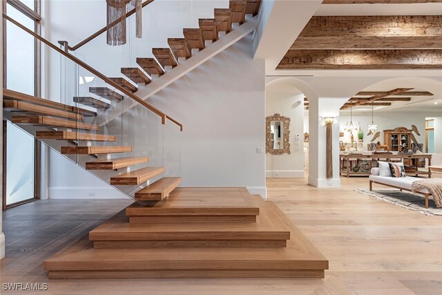 stairway featuring a towering ceiling, baseboards, arched walkways, and wood finished floors