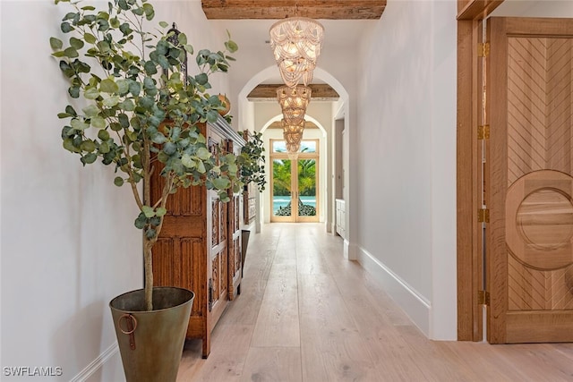 entryway featuring arched walkways, light wood-type flooring, a notable chandelier, and baseboards