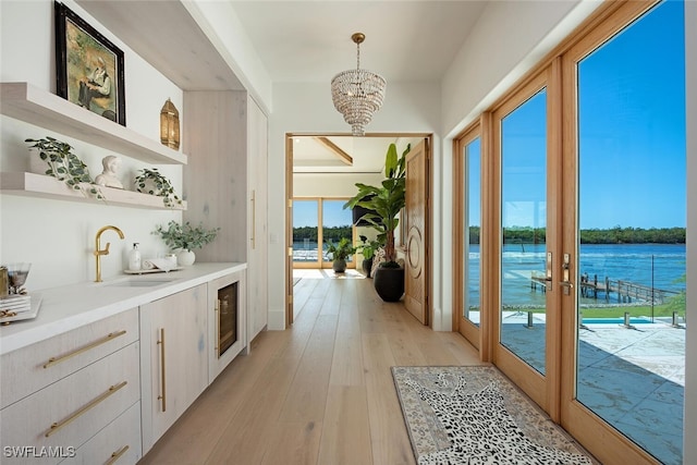 doorway with light wood-style flooring, wine cooler, a water view, an inviting chandelier, and a sink