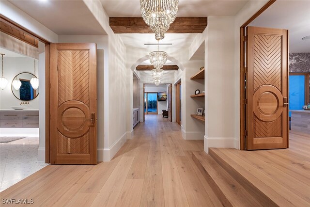 hall with built in shelves, a notable chandelier, baseboards, light wood finished floors, and beamed ceiling