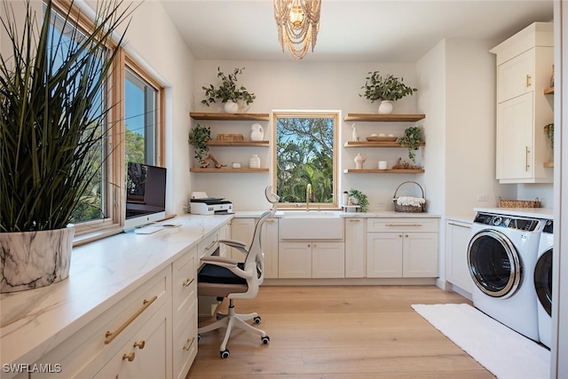 clothes washing area with cabinet space, washing machine and dryer, light wood-style flooring, and a sink