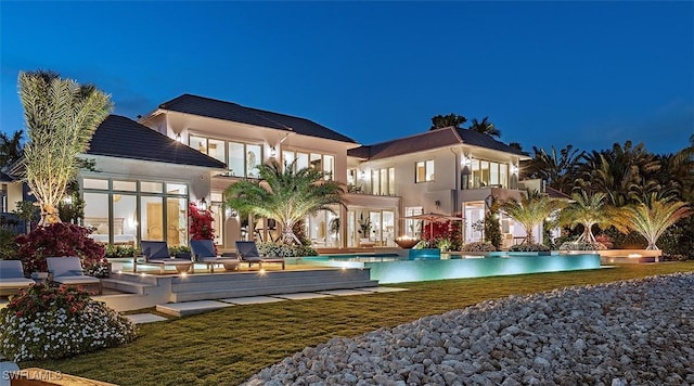 rear view of house with a lawn, an outdoor pool, a patio, and stucco siding