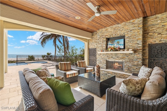 view of patio / terrace with an outdoor living space with a fireplace, ceiling fan, a water view, and a fenced in pool