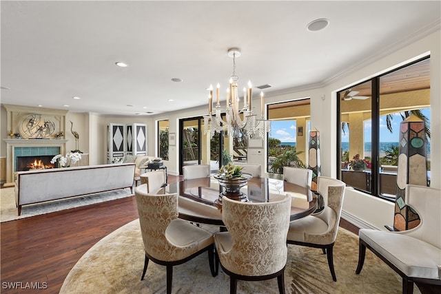 dining room with a tiled fireplace, a chandelier, dark wood-type flooring, and ornamental molding