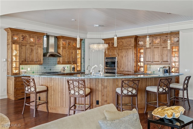 kitchen with dark hardwood / wood-style floors, wall chimney range hood, hanging light fixtures, and a breakfast bar