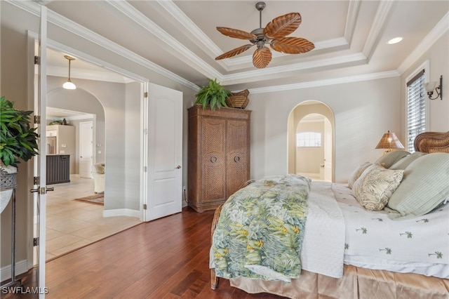 bedroom with hardwood / wood-style floors, ensuite bathroom, crown molding, ceiling fan, and a tray ceiling