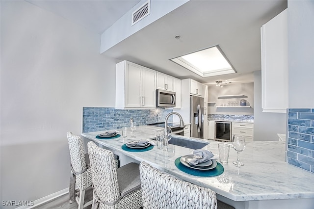 kitchen featuring kitchen peninsula, appliances with stainless steel finishes, light stone countertops, tasteful backsplash, and white cabinets