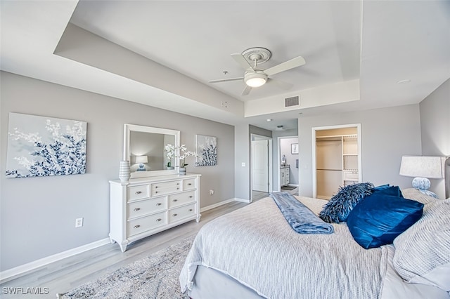 bedroom with a raised ceiling, ceiling fan, a spacious closet, light hardwood / wood-style floors, and a closet