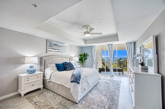 bedroom featuring access to exterior, a tray ceiling, light hardwood / wood-style flooring, and ceiling fan