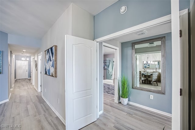 hall with light hardwood / wood-style flooring and an inviting chandelier